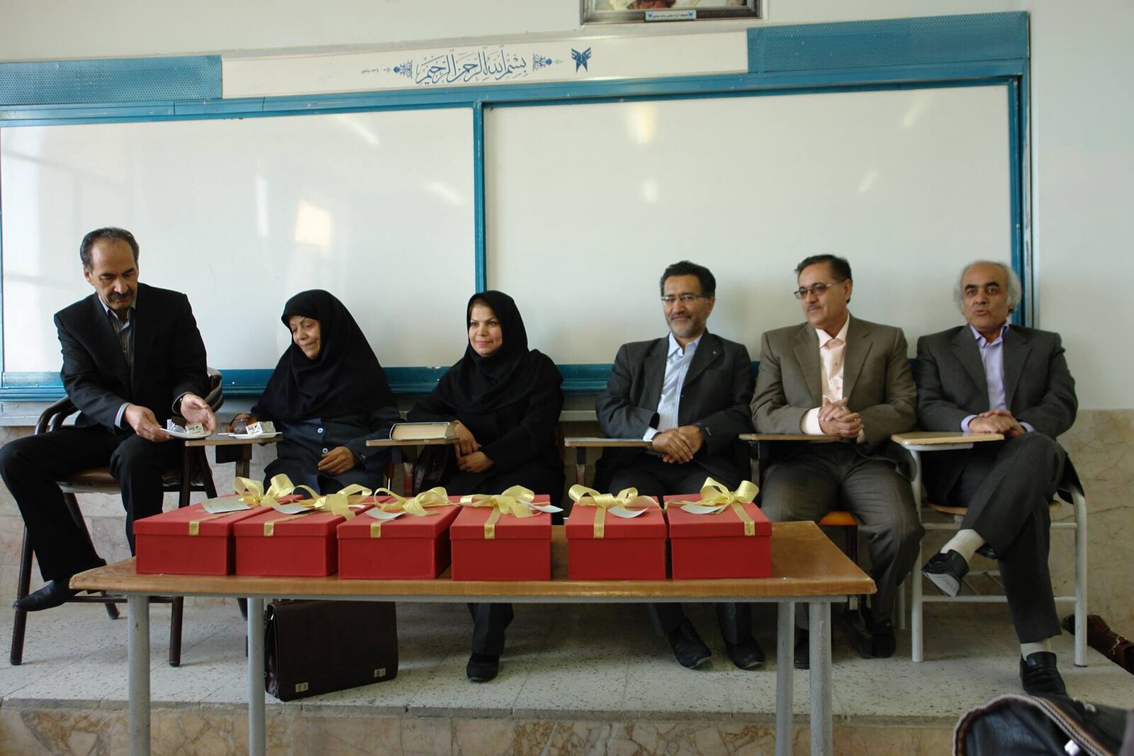 University Classroom | RaspGold English A group of people sit at a table with wrapped gifts in front of them, demonstrating communication skills during English.